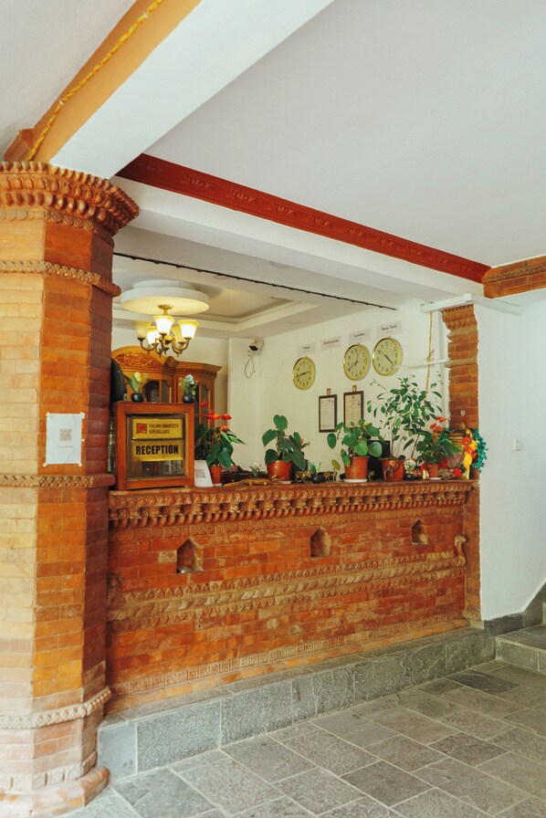 Un espace d’accueil avec un comptoir en briques, des plantes en pot et une horloge au mur.