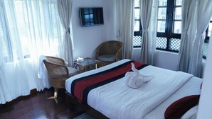 A hotel room with a large bed, a wicker chair, a small table, and a TV on the wall. - Ecohomekathmandu (Nagarjun)