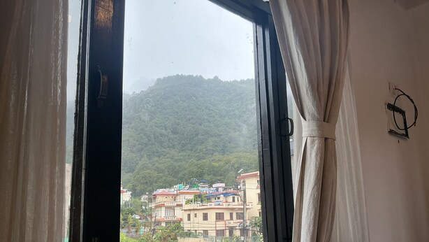 A room with a window overlooking a mountainous area with buildings. - Ecohomekathmandu (Nagarjun)