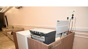 A reception desk with a Lenovo computer and a printer, a wooden counter, and a wall-mounted electrical outlet. - Hotel Nirvvana Residency (Varanasi)