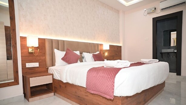 A modern hotel room with a large bed, wooden headboard, and bedside lamps. - Hotel Nirvvana Residency (Varanasi)