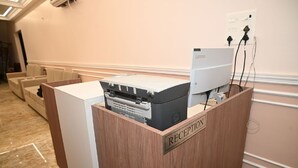 Una recepción con un computador Lenovo e impresora, un mostrador de madera y un enchufe en la pared.