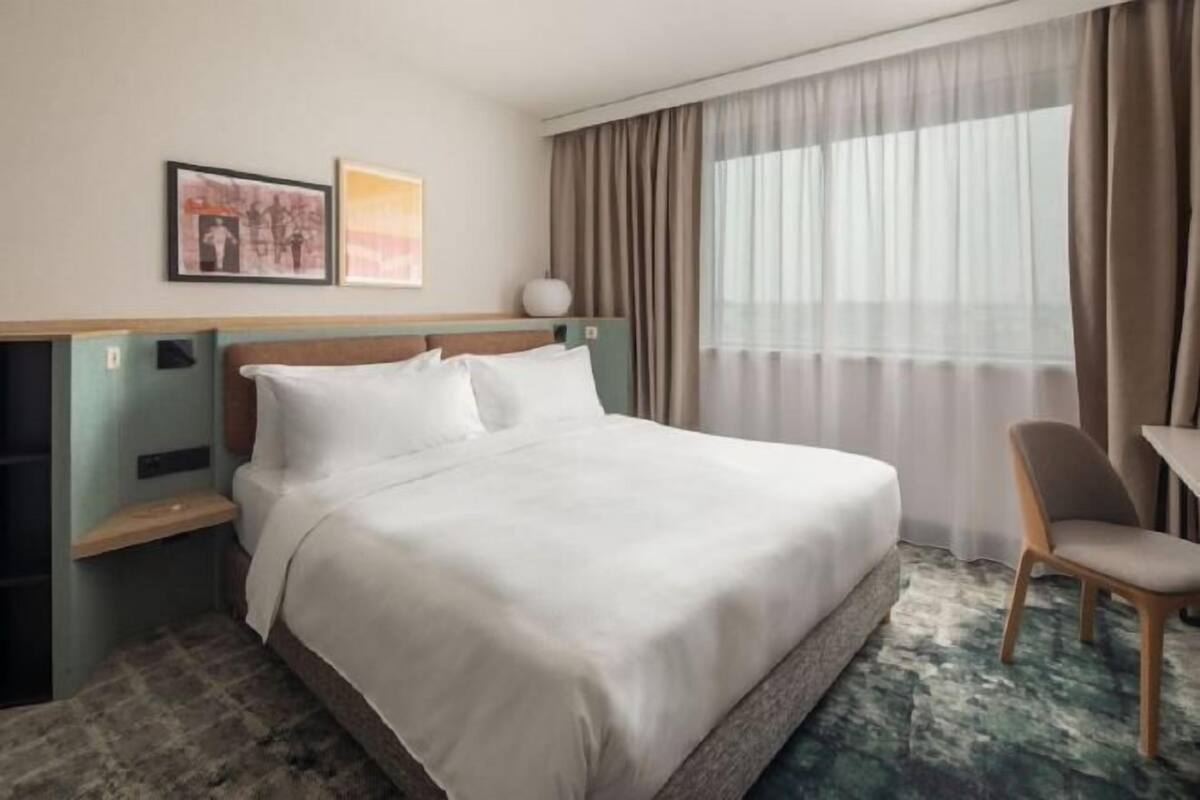A hotel room with a bed, a chair, a desk, and a window with curtains.