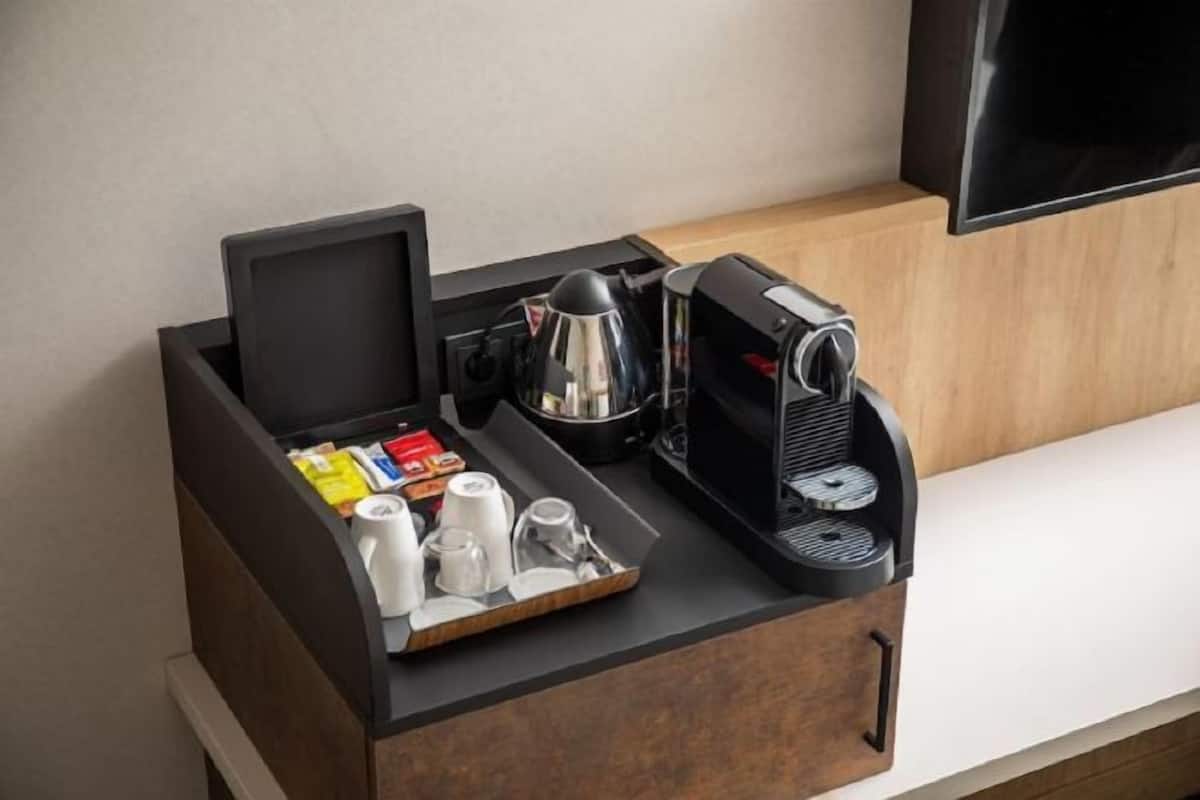 A compact coffee station with a coffee maker, a tray with cups and a kettle, and a drawer with a black interior.