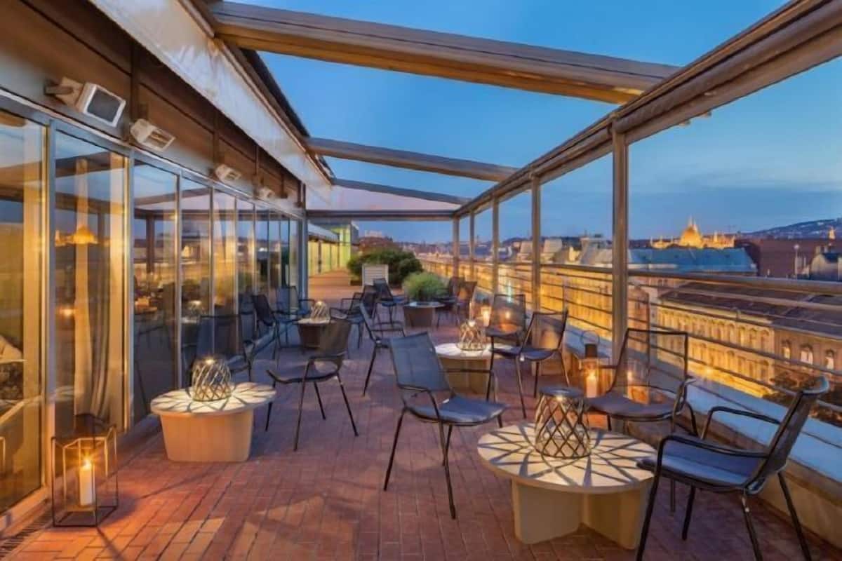 A rooftop terrace with glass walls, outdoor seating, and a view of a historic building.