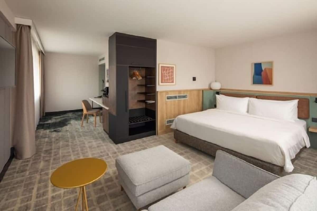 A hotel room with a bed, a desk, a chair, a small table, and a wardrobe.