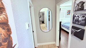 Un couloir avec un miroir, une porte avec un interrupteur et un lit recouvert d’une couverture bleue.