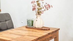 Een houten tafel met een witte vaas met roze bloemen en een groene kaars.