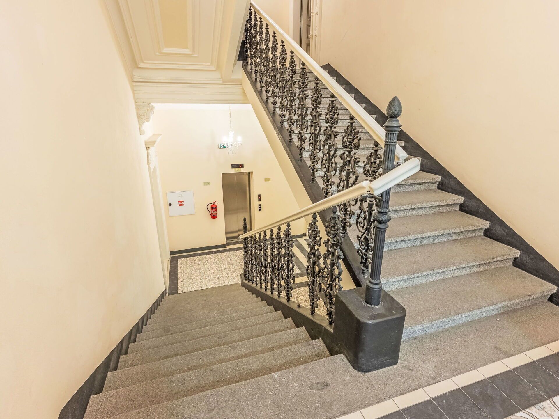 A staircase with ornate black balusters and a handrail, leading to an elevator.