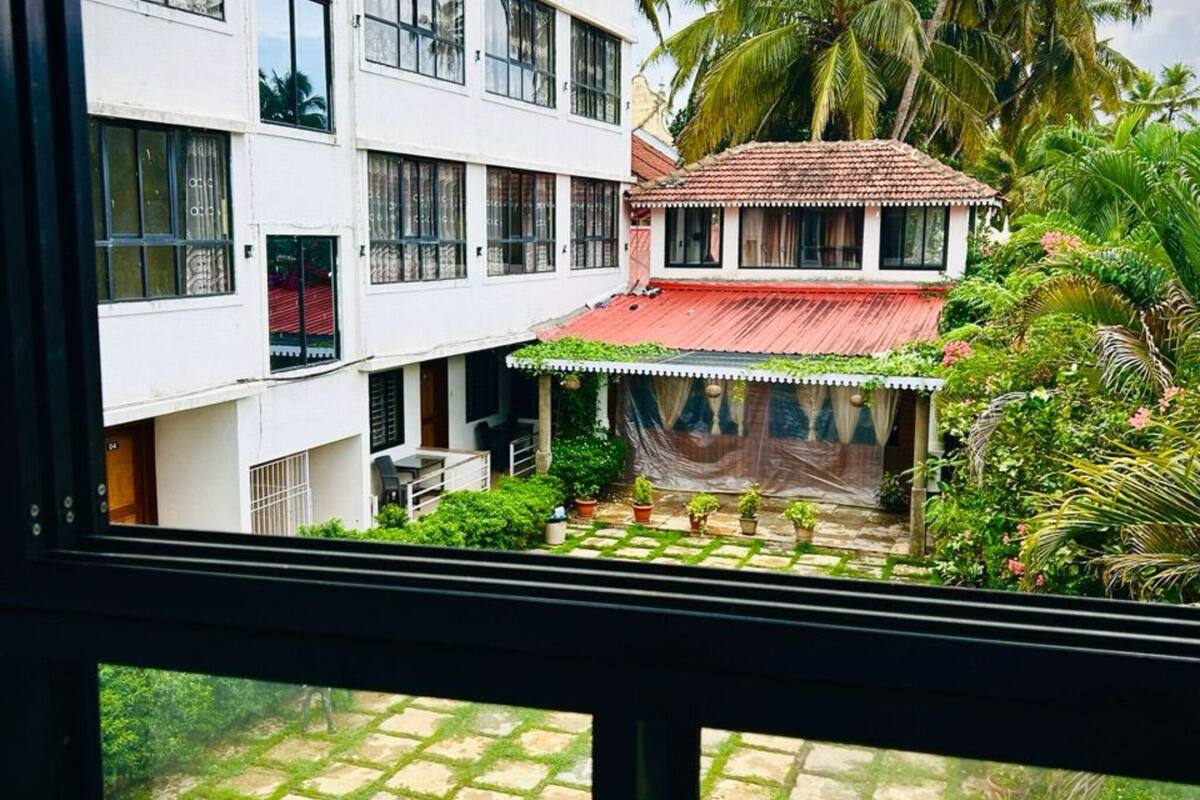 Un edificio de varios pisos con un patio, plantas en macetas y una estructura de techo rojo.