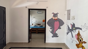 Een gang met een bed op de achtergrond, een muur met tekenfilmfiguren en een deur aan de linkerkant.