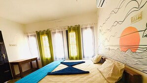 Een hotelkamer met een bed, gordijnen, een bureau en een muur met een muurschildering.