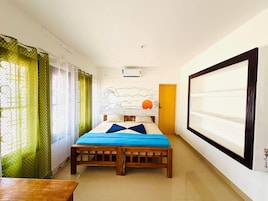 Una habitación con una cama, un banco de madera, un ventanal con cortinas, un aire acondicionado instalado en la pared y una puerta.