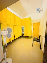 Una habitación con cortinas amarillas, un ventilador, una silla y una puerta.
