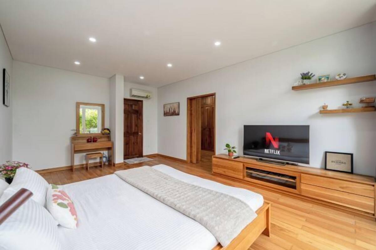 Ein modernes Schlafzimmer mit einem großen Bett, einer Holzkommode und einem Fernseher mit dem Netflix-Logo.