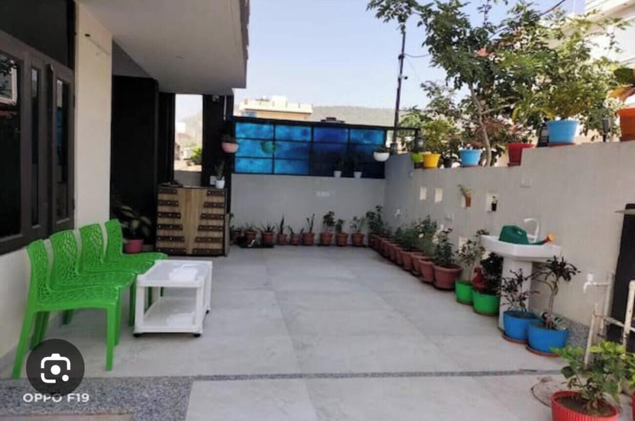 Un petit espace extérieur aménagé en patio, avec une chaise verte, une table blanche et divers pots de plantes.