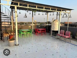 An outdoor patio with a pergola, seating area, and potted plants. - Uphar Homestay - Hotel & Restaurant (Jaipur)