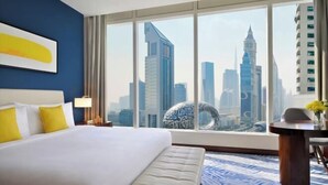A hotel room with a large bed, a desk, and a view of a city skyline. - voco DUBAI by IHG (Dubai)