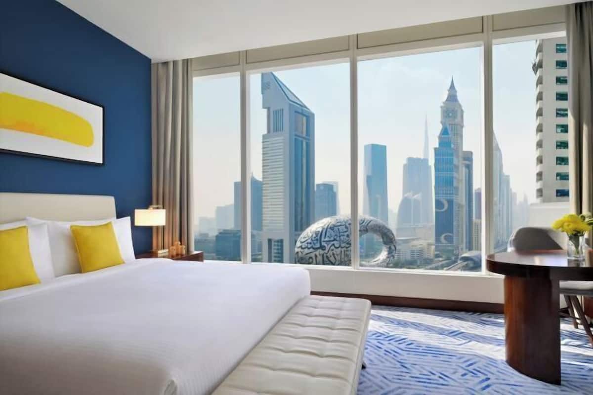 A hotel room with a large bed, a desk, and a view of a city skyline.
