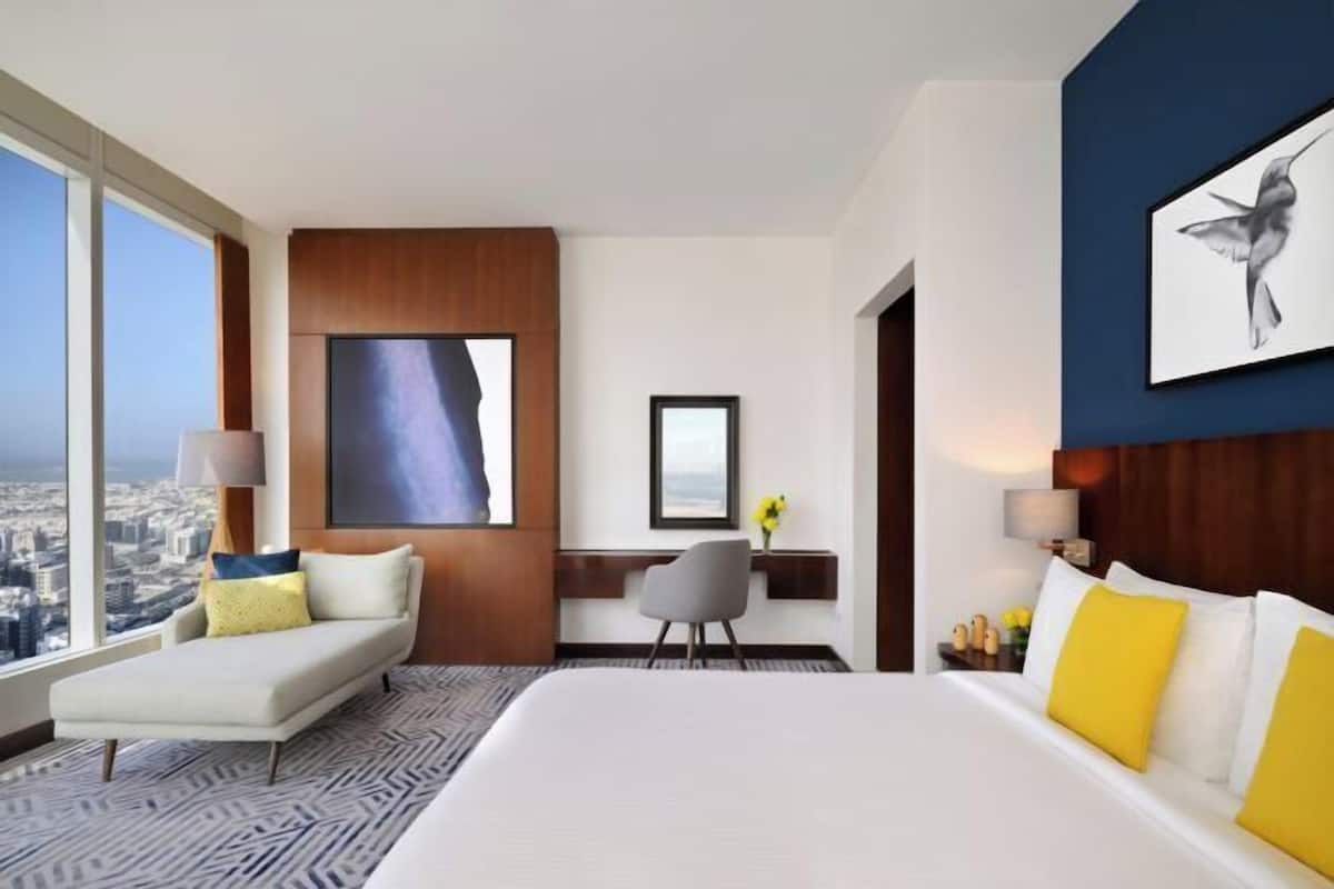 A hotel room with a large bed, a sofa, a desk, and a city view.