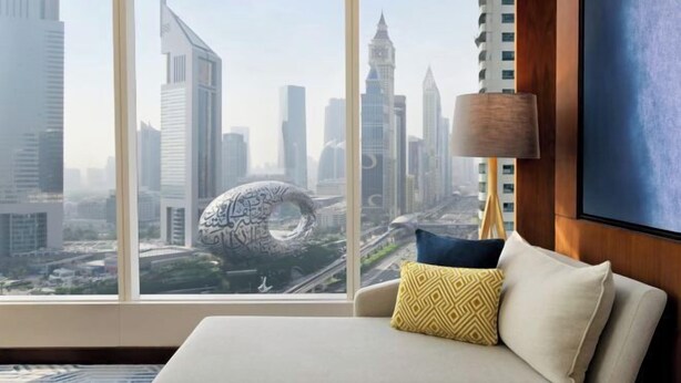 A modern interior with a sofa, patterned cushions, and a view of a cityscape through large windows. - voco DUBAI by IHG (Dubai)