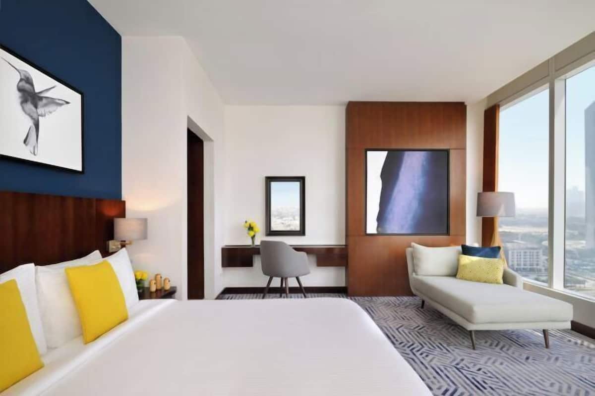 A hotel room with a large bed, a desk, a sofa, and a city view.