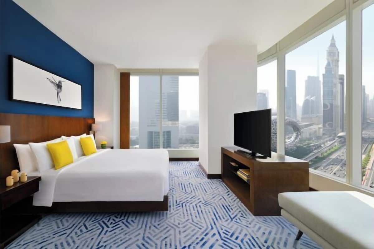 A modern hotel room with a large bed, a television, and a city view.