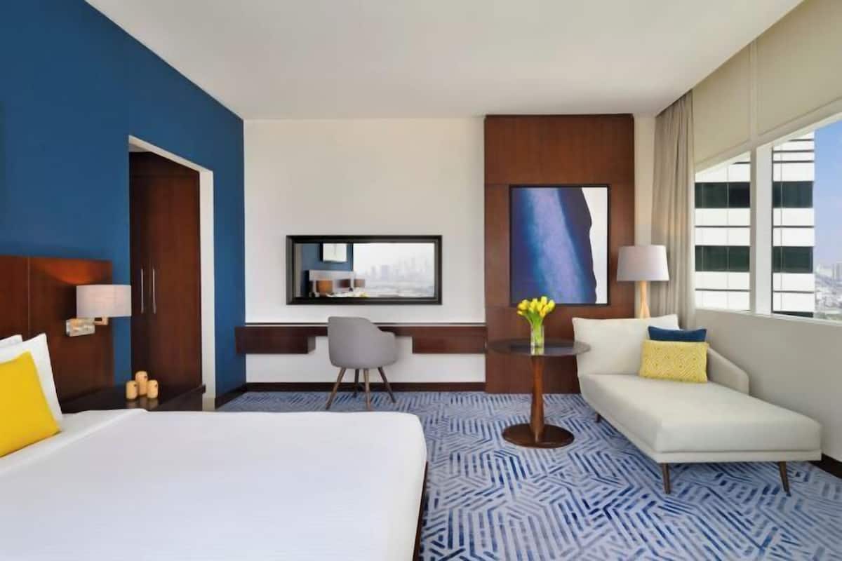 A hotel room with a bed, a sofa, a desk, a chair, a TV, and a window.