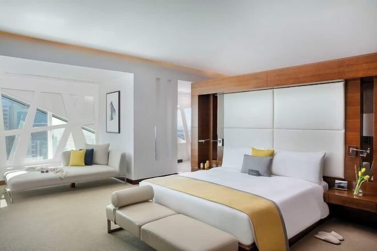 A modern hotel room with a large bed, a sofa, and a bench.