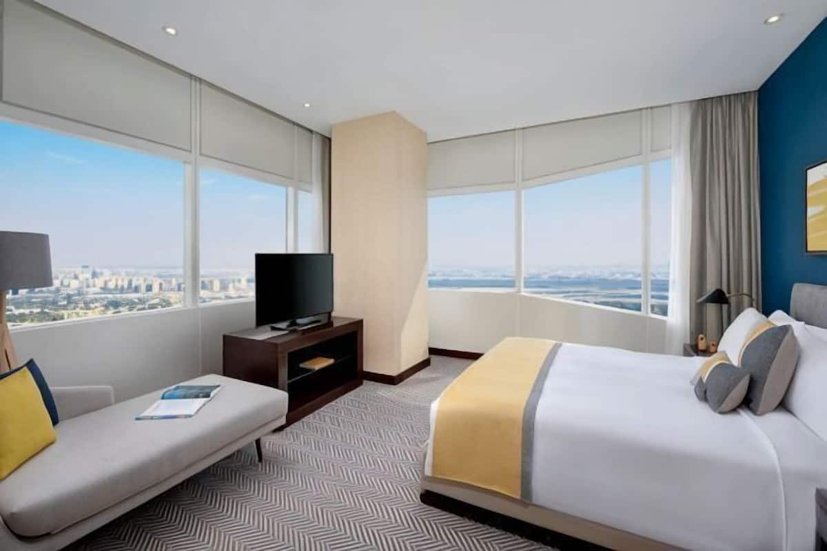 Ein Hotelzimmer mit Bett, einer Couch, einem Fernseher und einem großen Fenster mit Blick auf die Stadt.