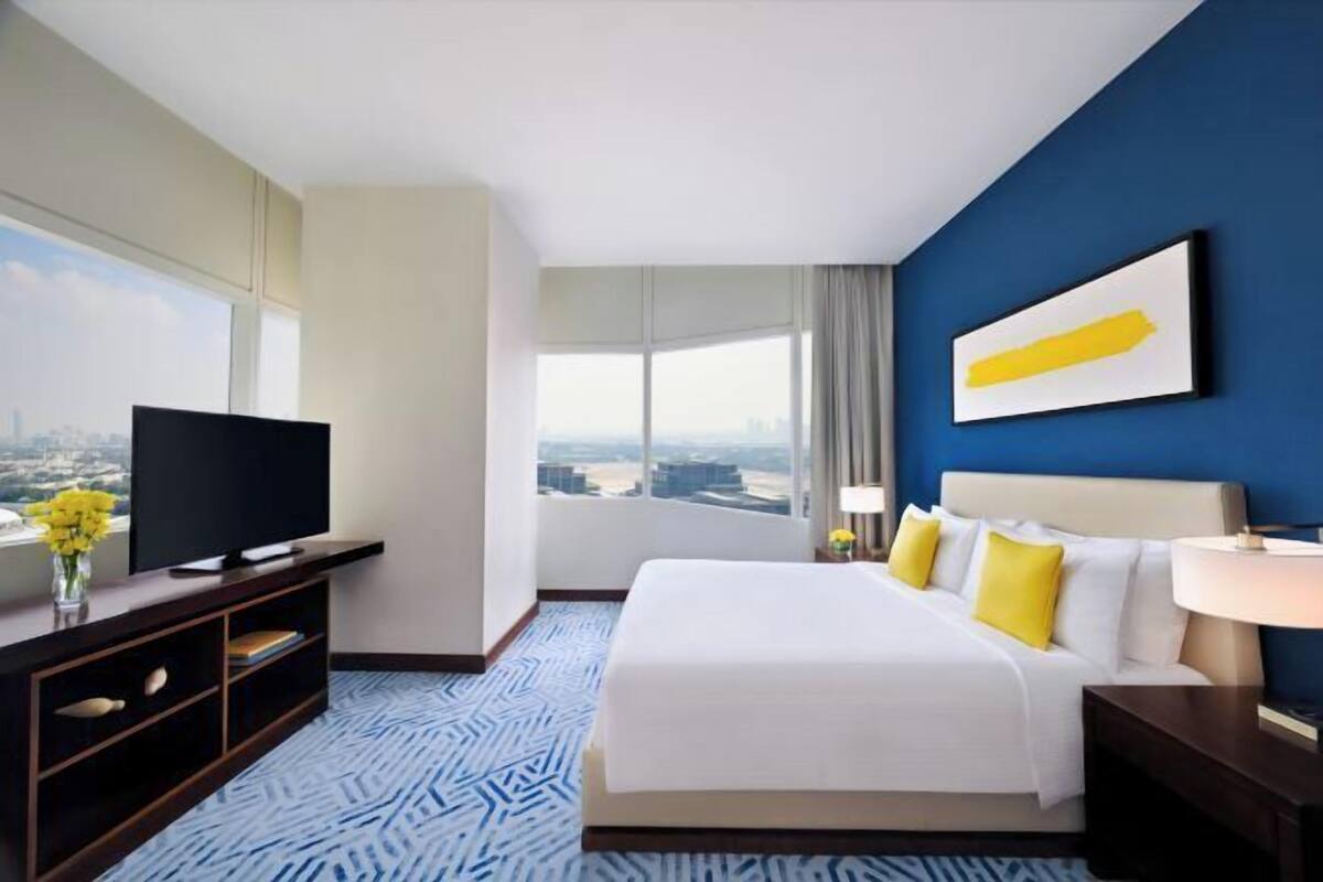 A hotel room with a bed, a TV, a city view, and a blue wall.