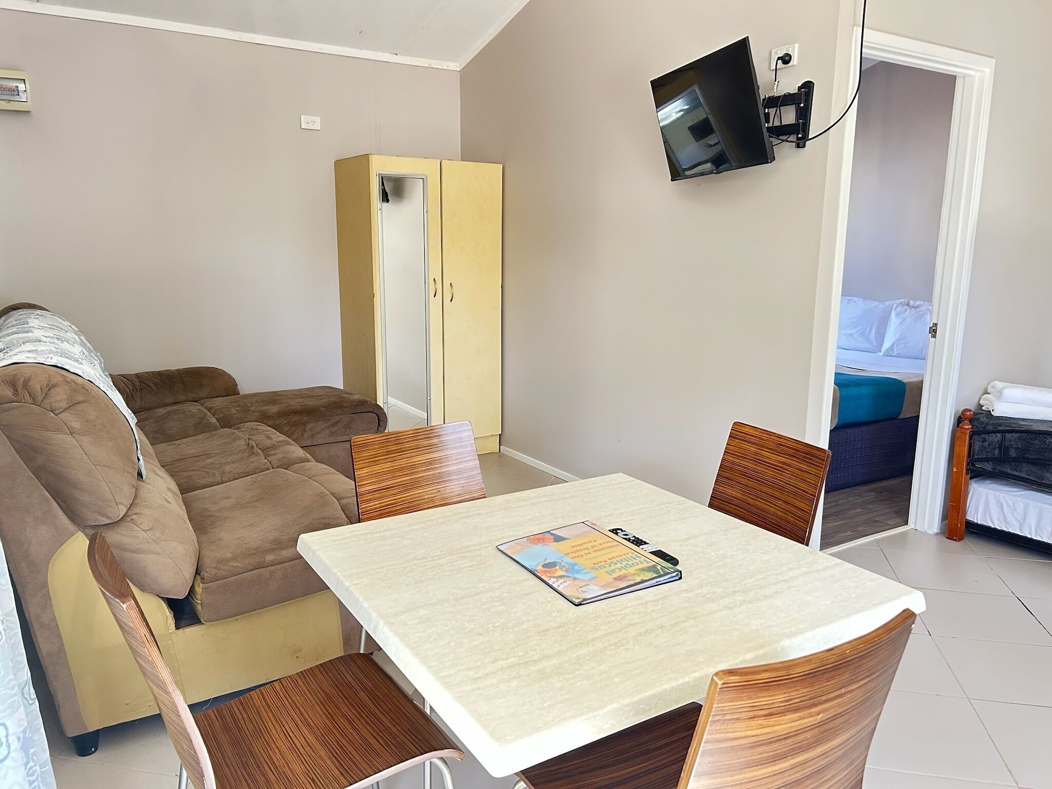 A room with a sofa, a table with a magazine, a TV mounted on the wall, and a wardrobe.