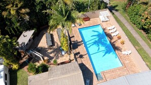 Vista aérea de un patio trasero con piscina, sillas de descanso y palmeras.