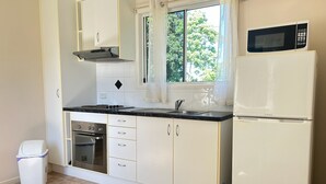 Una cocina con armarios blancos, encimera negra, horno de acero inoxidable, microondas y ventana con vistas a árboles.