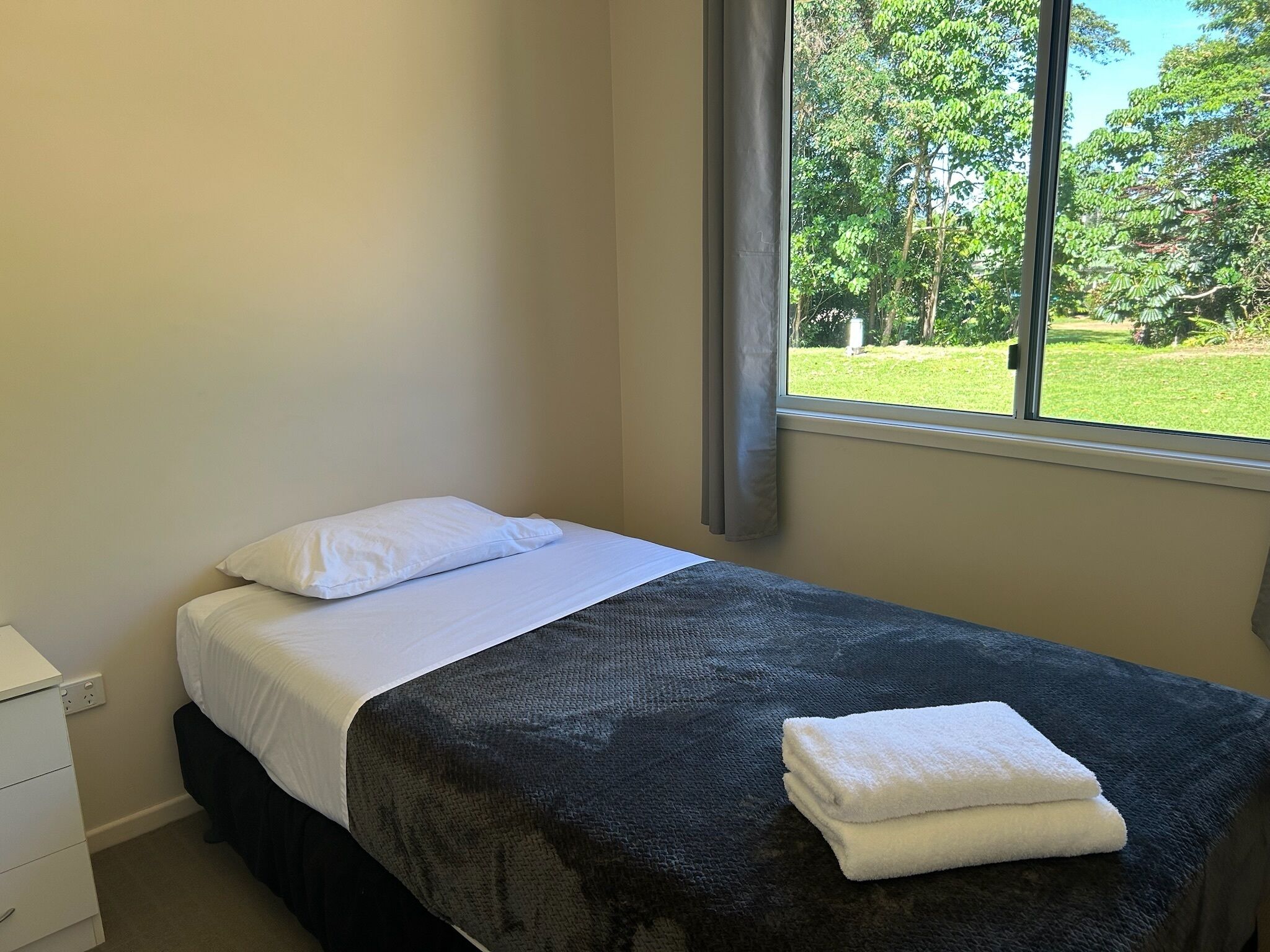A single bed with white bedding, a dark blanket, and a folded white towel.