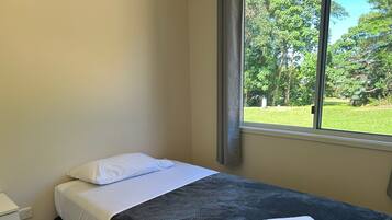 A single bed with white bedding, a dark blanket, and a folded white towel.