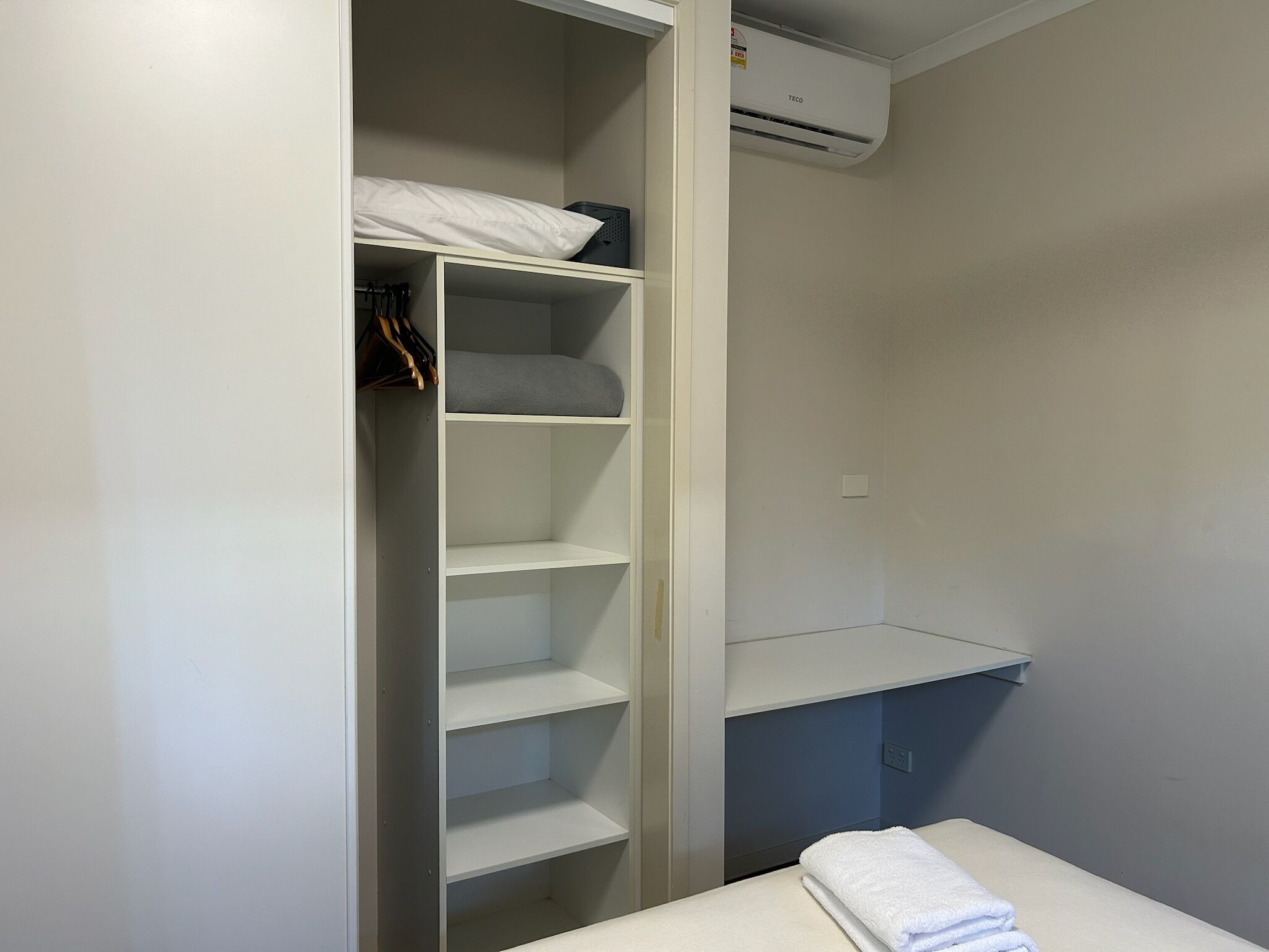 A closet with shelves, a hanging rack, and a folded towel on a table.