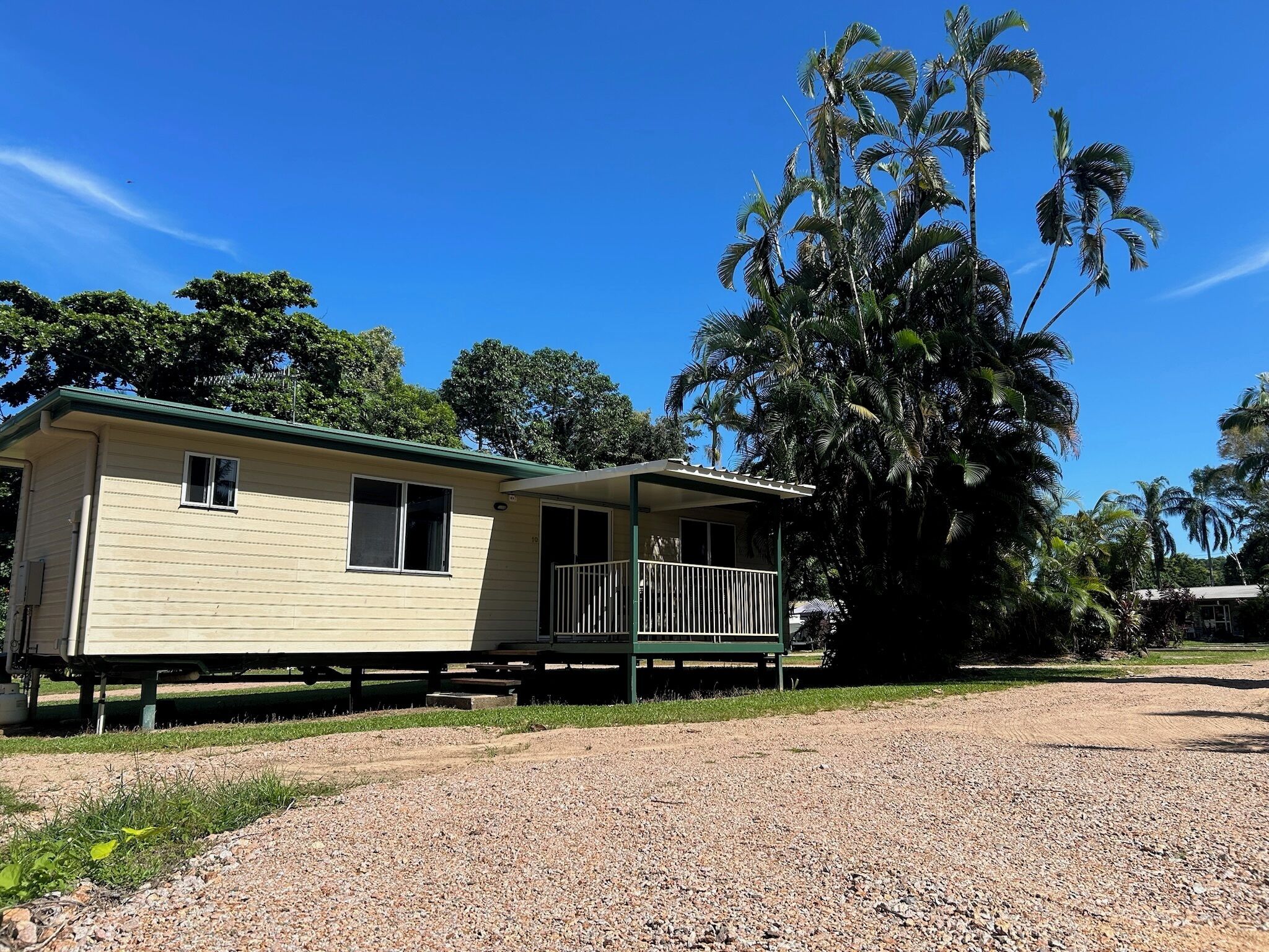 A single-story mobile home with a porch, surrounded by gravel and greenery.