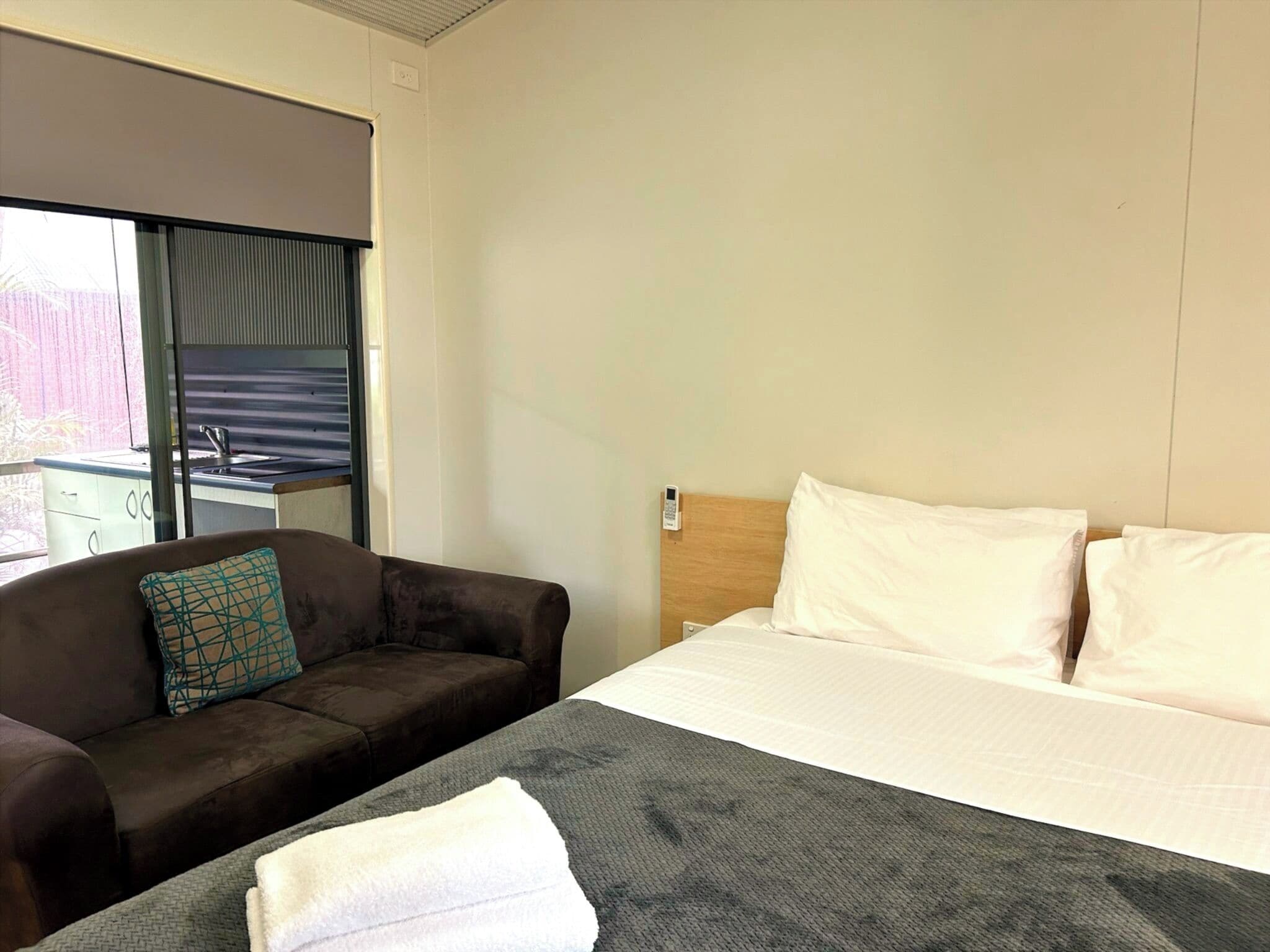 Quarto de hotel com cama, sofá, janela com cortinas e uma pequena cozinha.