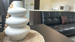 Una sala moderna con un sofá de cuero negro, una escultura blanca con textura sobre una mesa y una cocina al fondo.