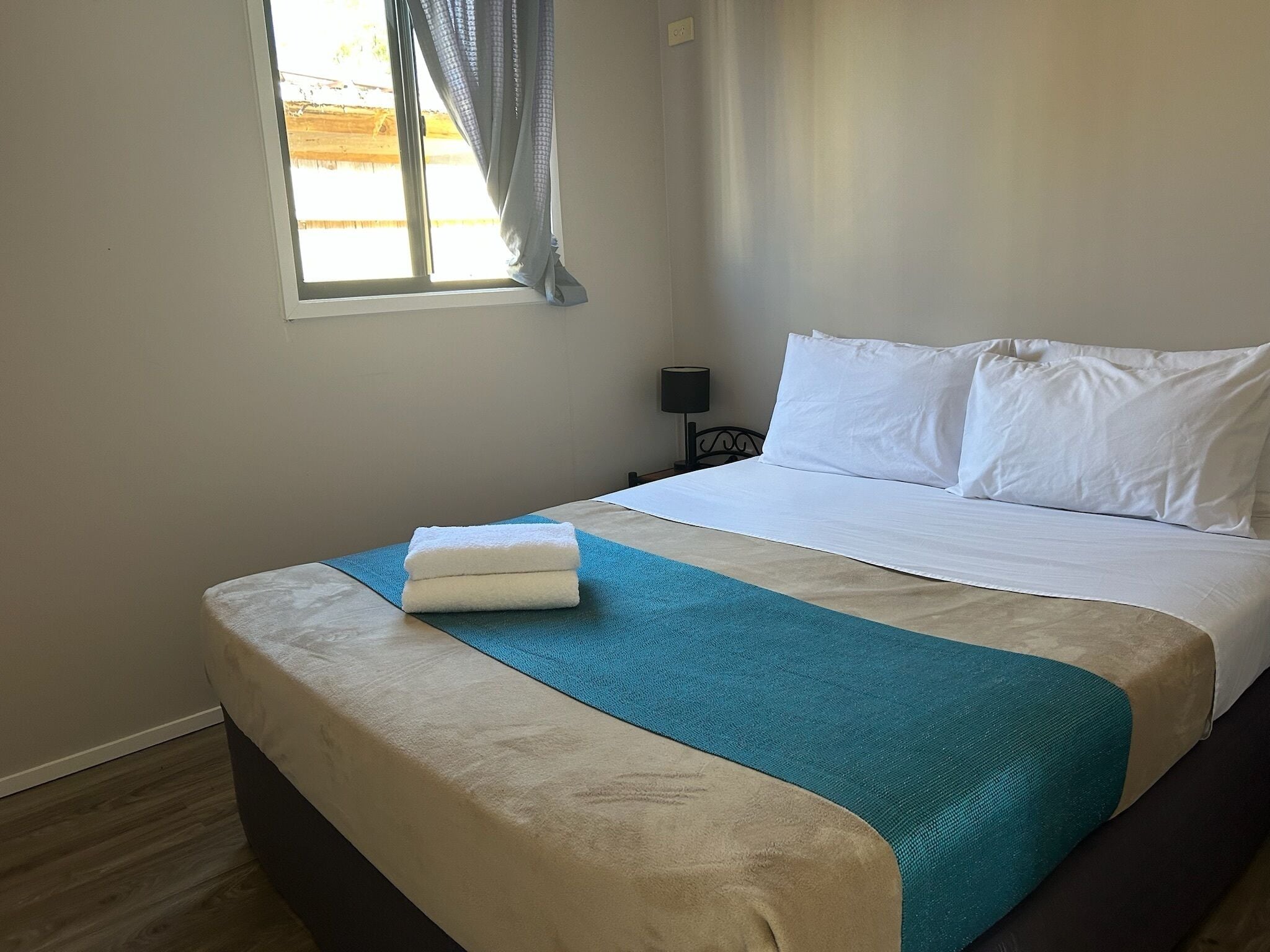 Una cama bien tendida con sábanas blancas, un cojín de acento azul y una toalla blanca doblada.