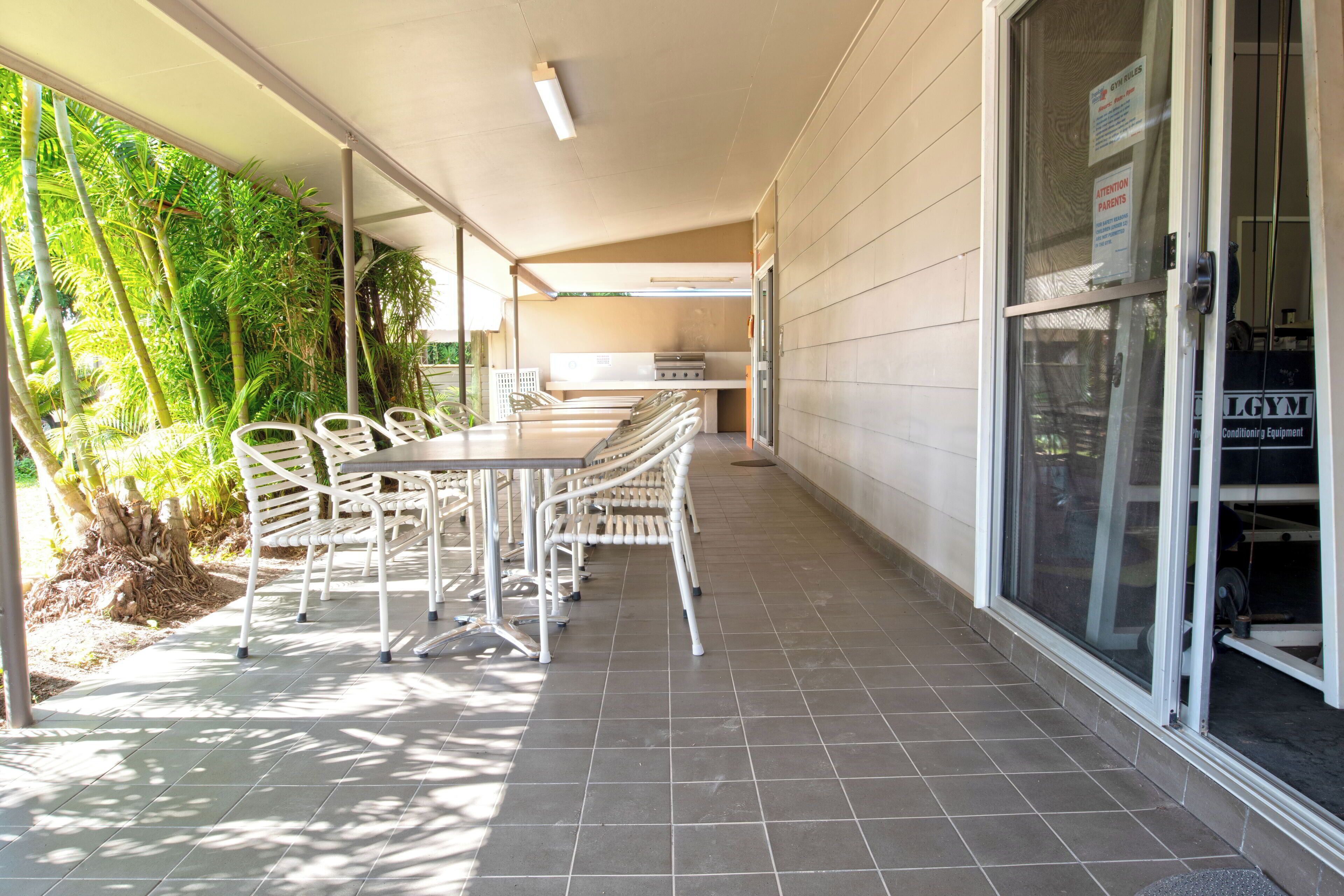 A covered patio with a table and chairs, a grill, and a door with a sign.