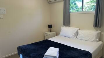A bedroom with a bed, a nightstand, an air conditioning unit, and a window with curtains.