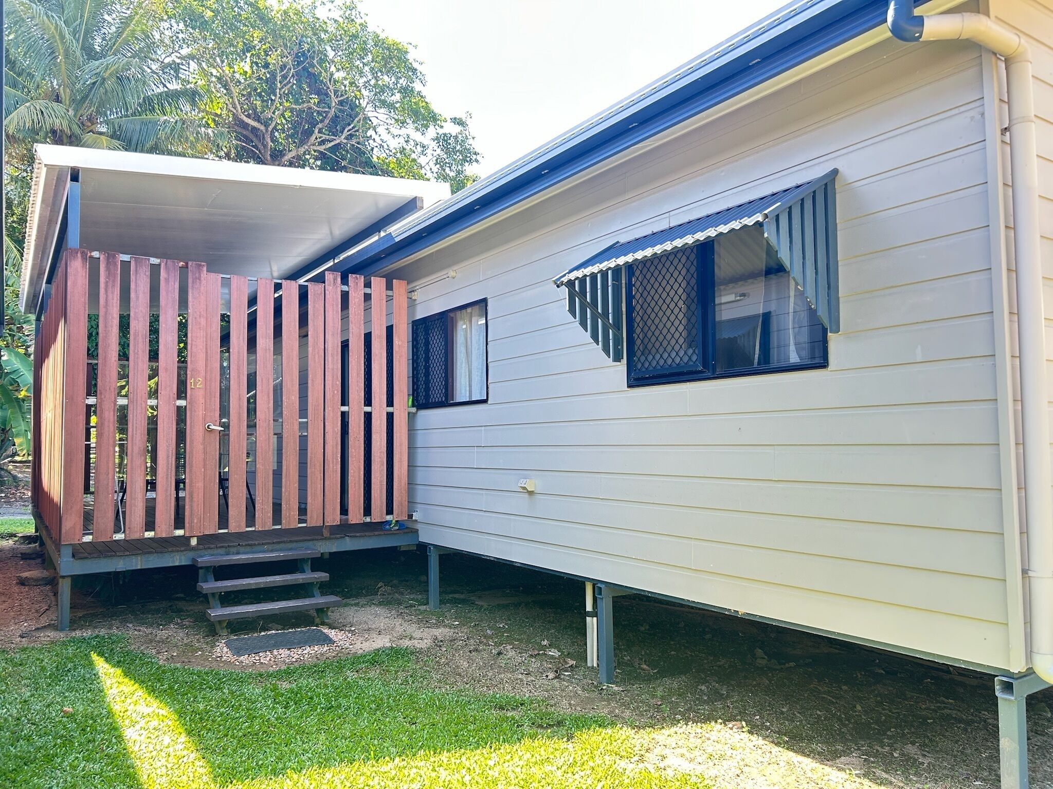 A mobile home with a wooden deck, a small porch, and a window with a mesh screen.