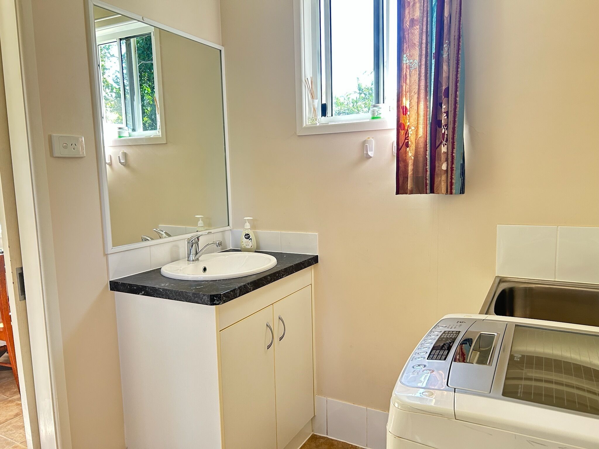 Une salle de bain équipée d’un lavabo, d’un miroir, d’une fenêtre et d’un lave-linge.