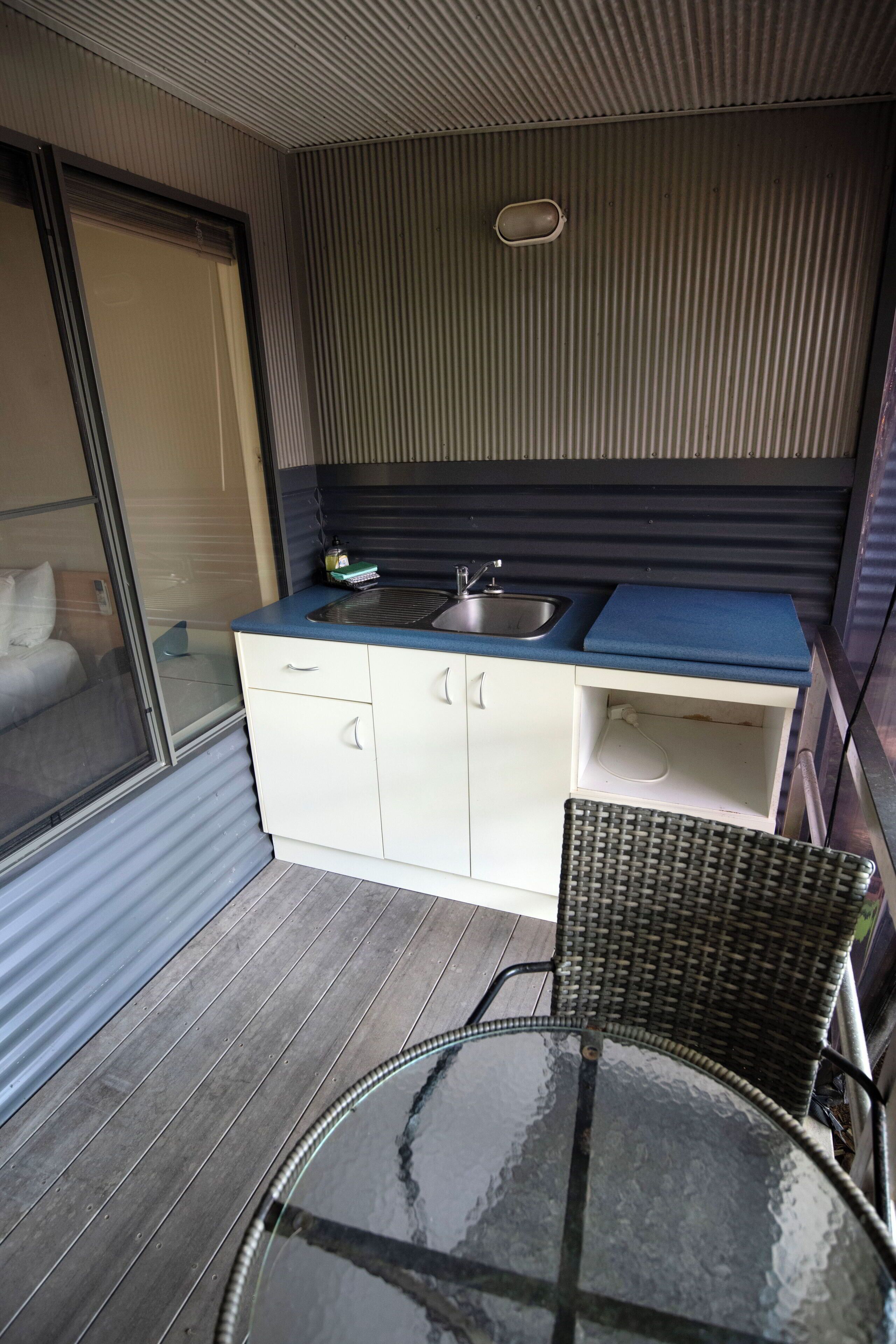 Una kitchenette compacta con un lavamanos, una pequeña encimera y una mesa de vidrio.
