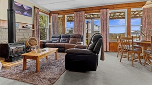A cozy living room with a fireplace, leather sofa, and a dining area with wooden chairs. - Sunny Hilltop Red Bach w Lake and Mountain Views (Taupō)