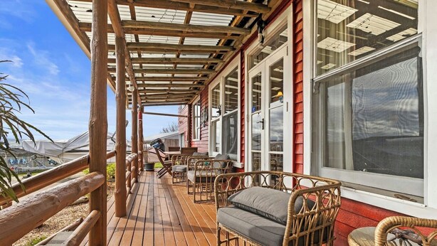 A covered deck with wicker furniture and a view of the ocean. - Sunny Hilltop Red Bach w Lake and Mountain Views (Taupō)