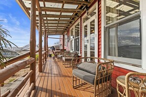 A covered deck with wicker furniture and a view of the ocean. - Sunny Hilltop Red Bach w Lake and Mountain Views (Taupō)