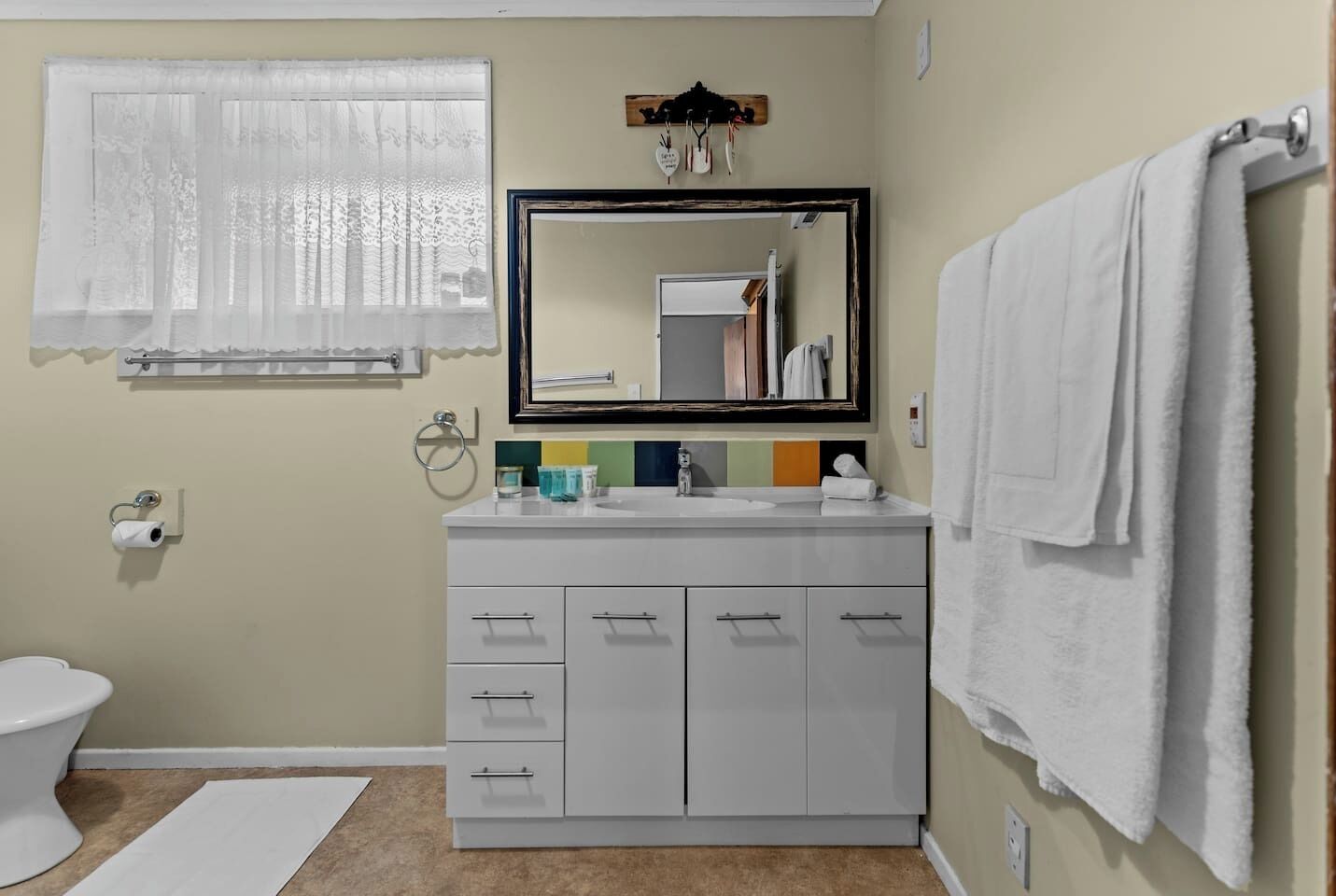 Baño con inodoro, lavabo, espejo y barra para toallas.